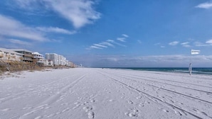 Praia coberta de neve com pegadas, uma bandeira e edifícios ao fundo.