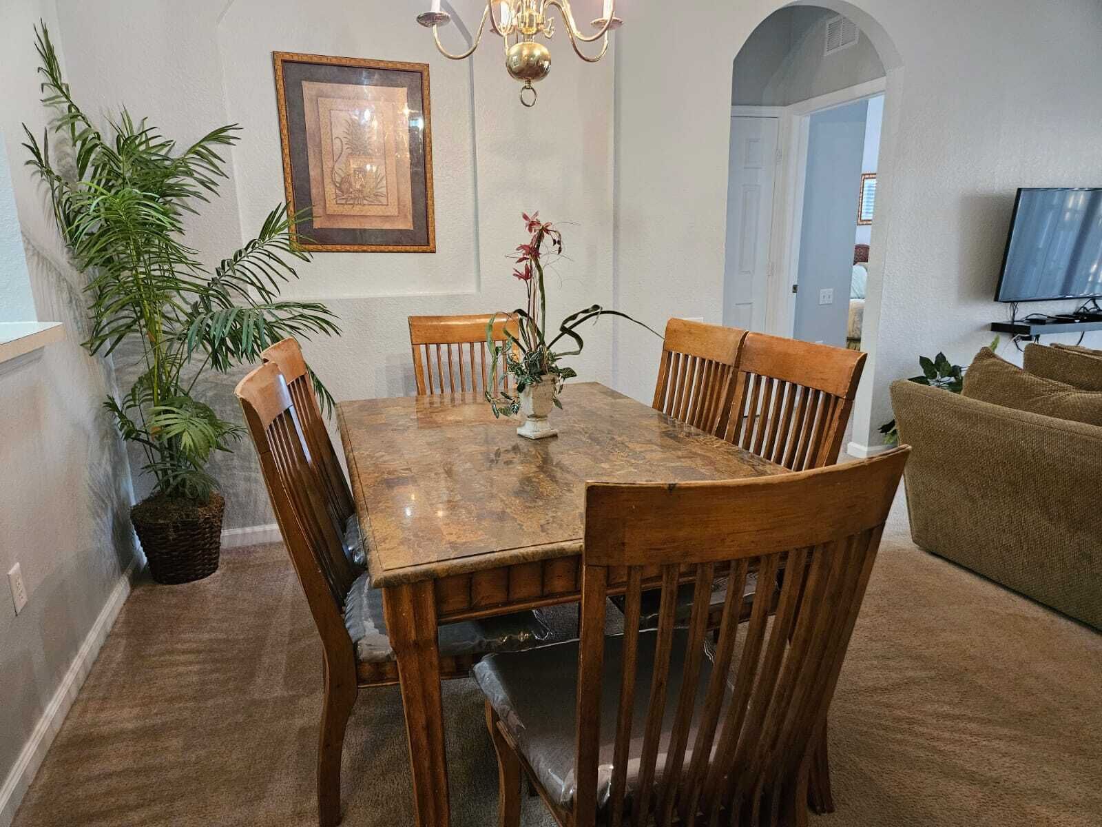 Un comedor con mesa y sillas de madera, una lámpara de araña, un cuadro en la pared y una planta en maceta.