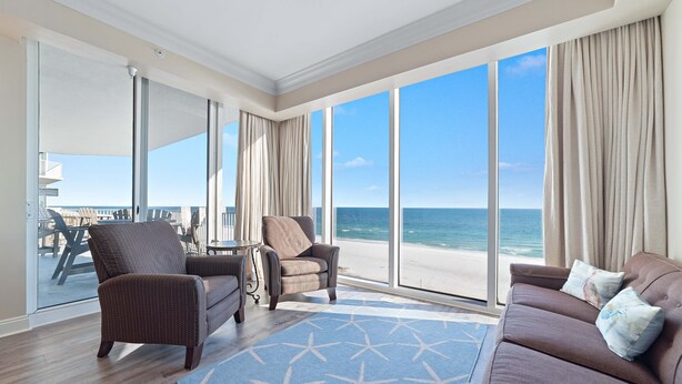 A spacious room with a large window overlooking the beach, a sofa, two armchairs, and a small table. - Mediterranean West 601W | Next to Florabama | Heated Indoor Pool w/Swim-Thru | My Beach Getaways (Pensacola)