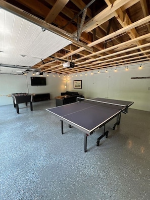 A ping pong table in a room with a high ceiling and exposed beams, a projector, and a small seating area. - Modern cottage located near Sister Bay with Game Room and Fire Pit (Ellison Bay)
