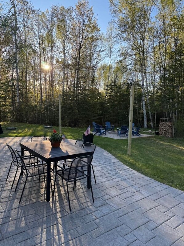 An outdoor patio with a table and chairs, surrounded by a wooded area.