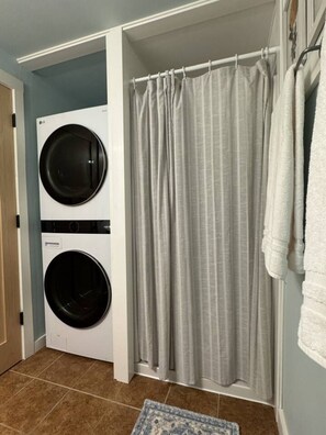 A laundry room with two stacked washers and dryers, a shower curtain, and a towel rack.
