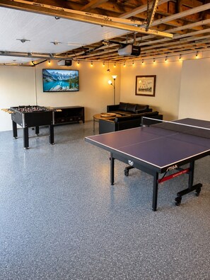 A recreational area with a foosball table, ping pong table, and a sofa.