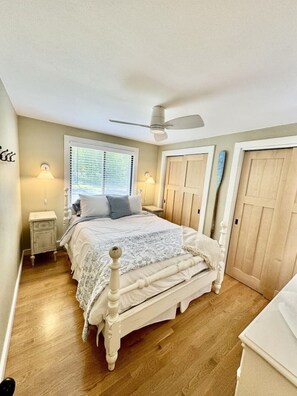 A bedroom with a bed, a ceiling fan, a window with blinds, a nightstand, and a door. - Modern cottage located near Sister Bay with Game Room and Fire Pit (Ellison Bay)