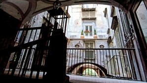 Blick durch ein vergittertes Fenster mit Balkon, zeigt ein Gebäude mit Balkonen und einer Treppe.