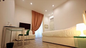 Ein modernes Hotelzimmer mit einer Couch, einem Glastisch mit Stühlen, einem Fernseher und einem großen Fenster mit Vorhängen.