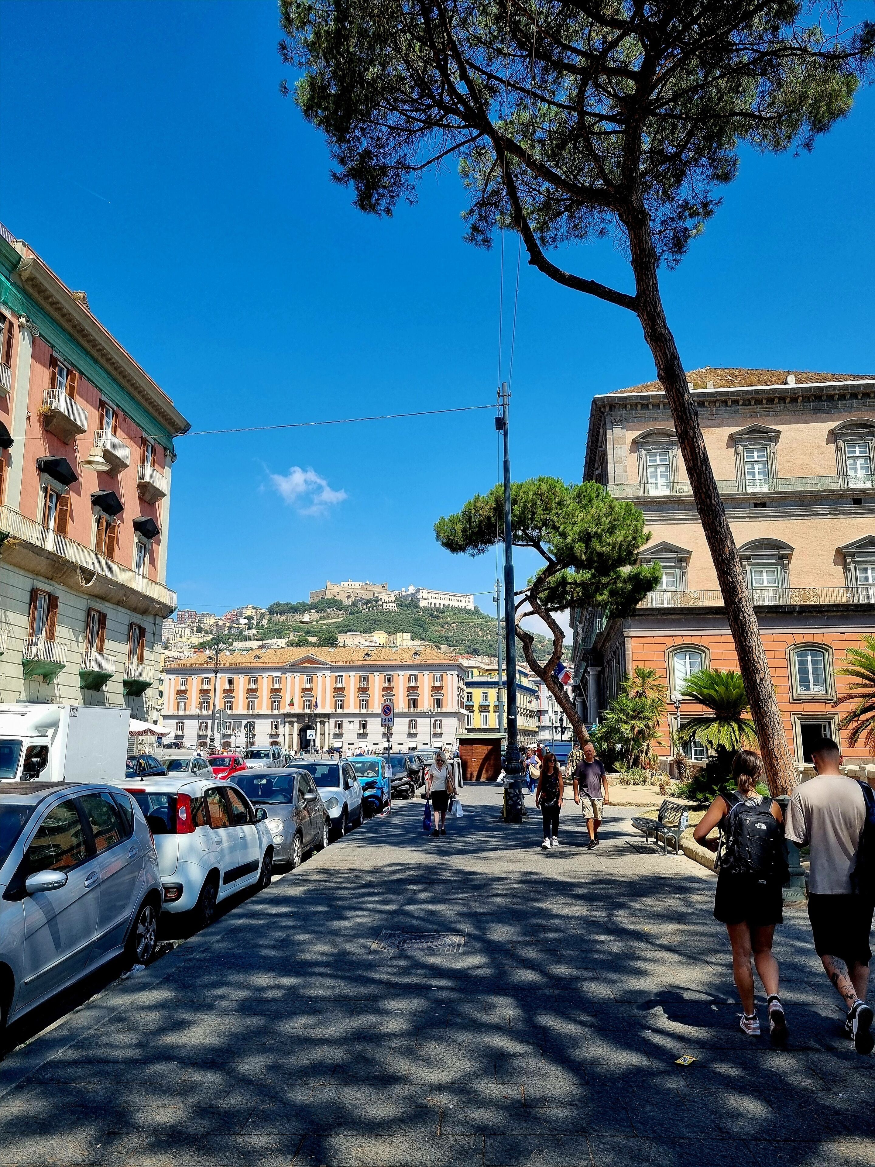 A street with parked cars and pedestrians.