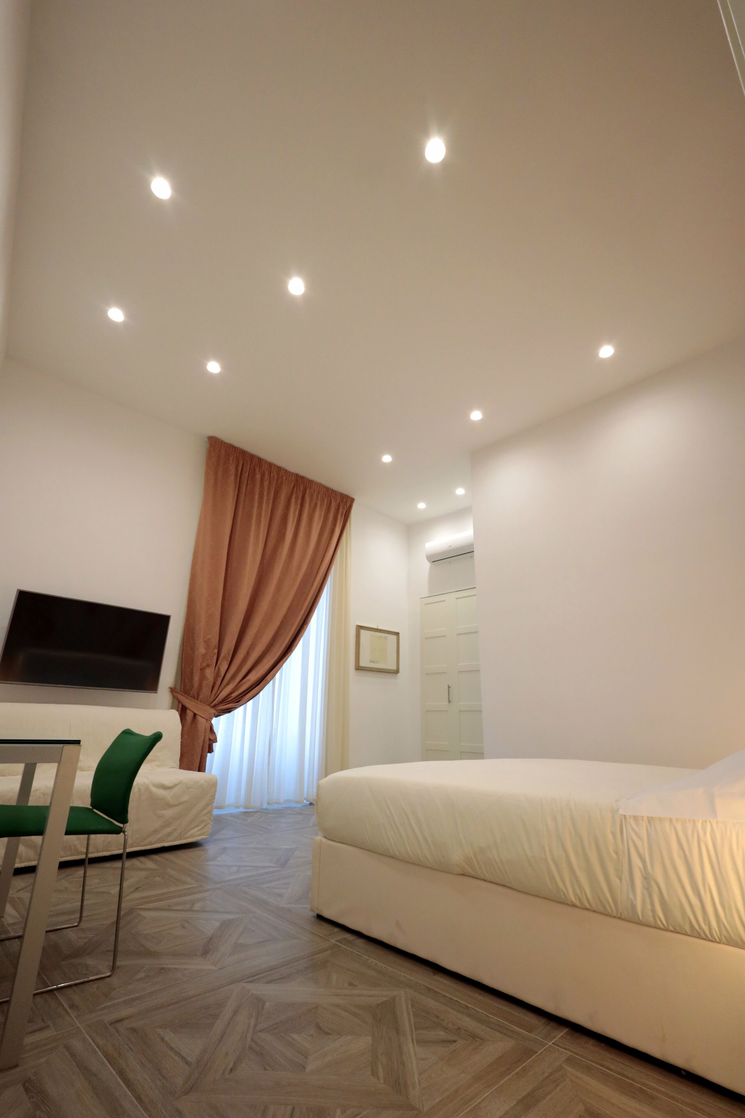 A hotel room with a bed, a chair, a TV, and a window with curtains.