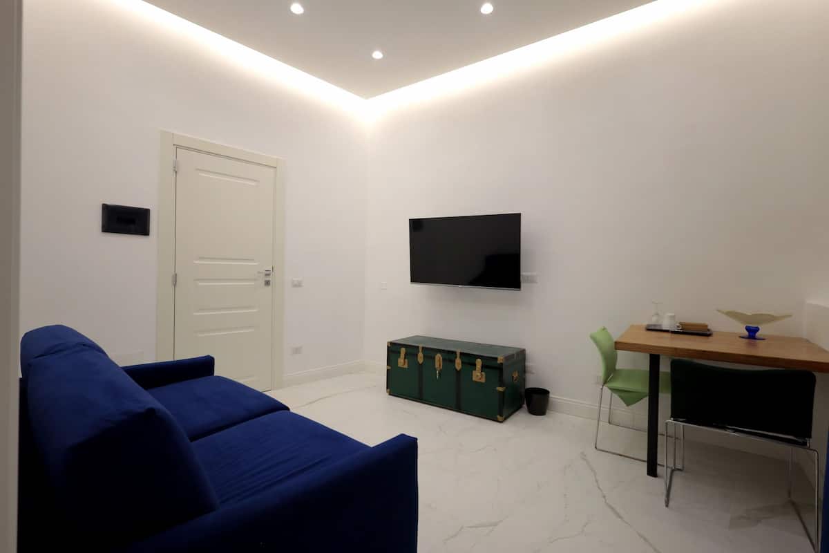 Ein modernes Wohnzimmer mit einem blauen Sofa, einer grünen Kommode, einem Holztisch und einem an der Wand befestigten Fernseher.