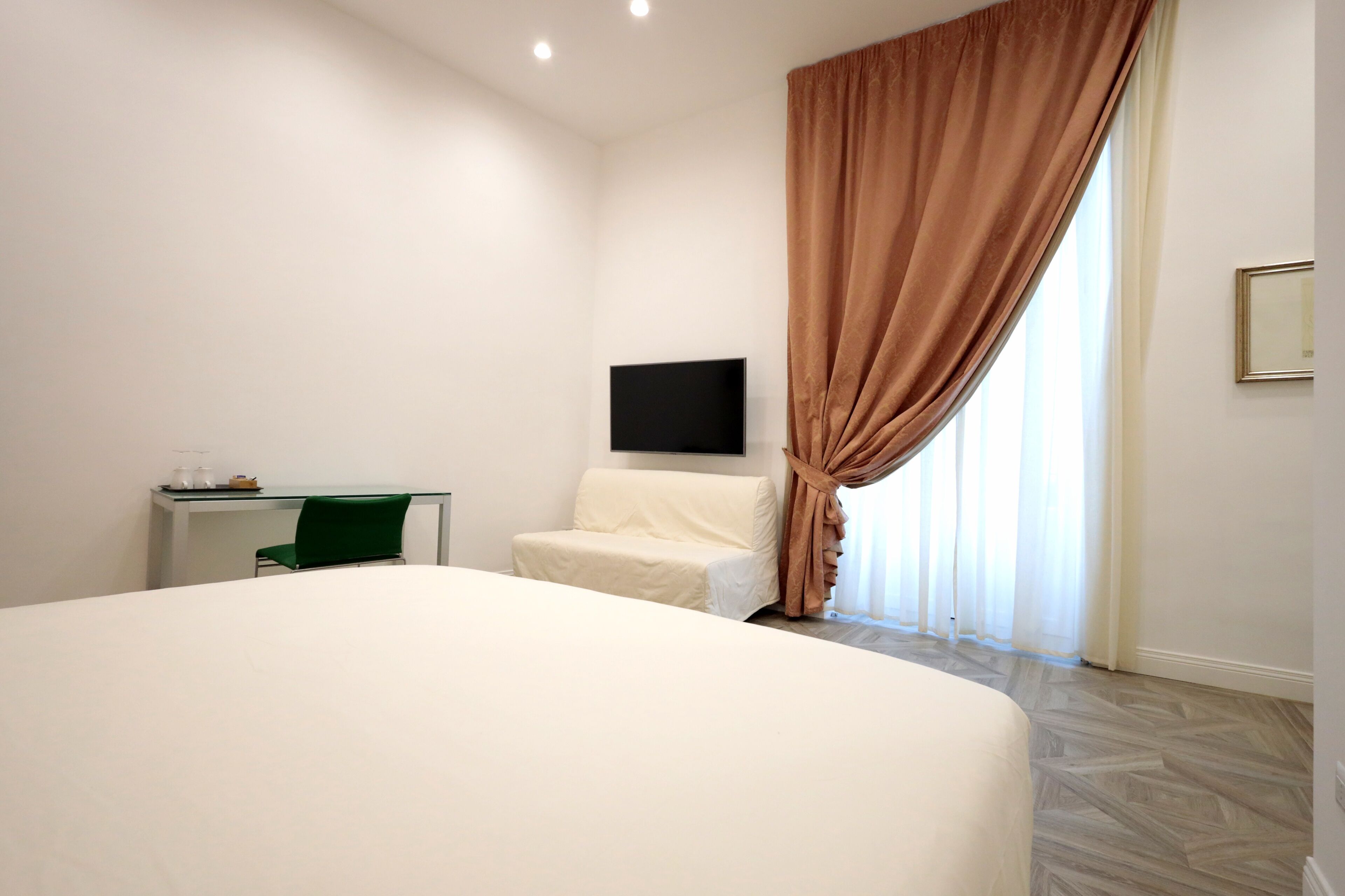 Une chambre d’hôtel avec un grand lit, un bureau avec une chaise, un téléviseur à écran plat fixé au mur et une fenêtre avec des rideaux.