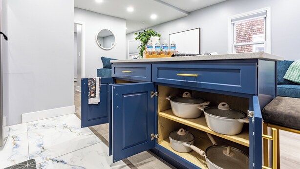 A modern kitchen with blue cabinets, a marble floor, and a countertop with water bottles and a plant. - Comfort Meets Style 3-bedroom apartment with Wi-Fi and Parking Close to NYC (New Rochelle)