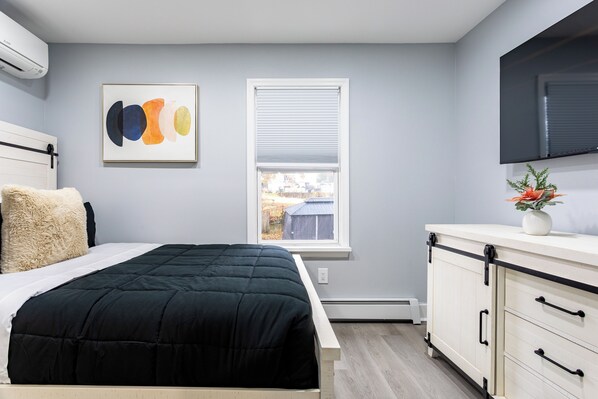 A bedroom with a bed, a window, a mounted TV, and a wall-mounted artwork.