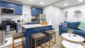 A modern kitchen with blue cabinets, a central island, and a seating area with a blue sofa and a coffee table. - Comfort Meets Style 3-bedroom apartment with Wi-Fi and Parking Close to NYC (New Rochelle)