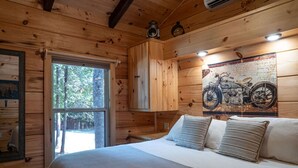 Ein Schlafzimmer einer Holzhütte mit einem Bett, einem Fenster, einem Motorradposter und einem Schrank.