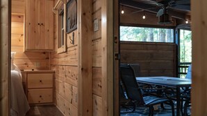 Innenansicht einer Holzhütte mit Essbereich, Deckenventilator und Fenster mit Blick auf Grünflächen.
