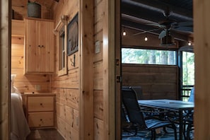 Innenansicht einer Holzhütte mit Essbereich, Deckenventilator und Fenster mit Blick auf Grünflächen.