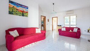 A spacious living room with two red sofas, a painting on the wall, and a large window providing natural light. - Arangiu 1 by Interhome (Muravera Villaputzu)