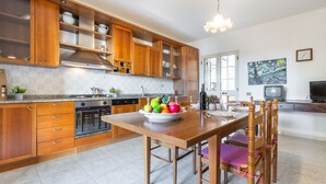 A modern kitchen with wooden cabinets, a dining table with chairs, and a fruit bowl. - Arangiu 1 by Interhome (Muravera Villaputzu)