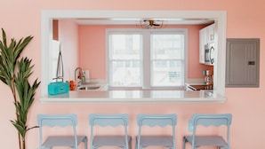 A kitchen with a pink wall, a white countertop, and four blue chairs.