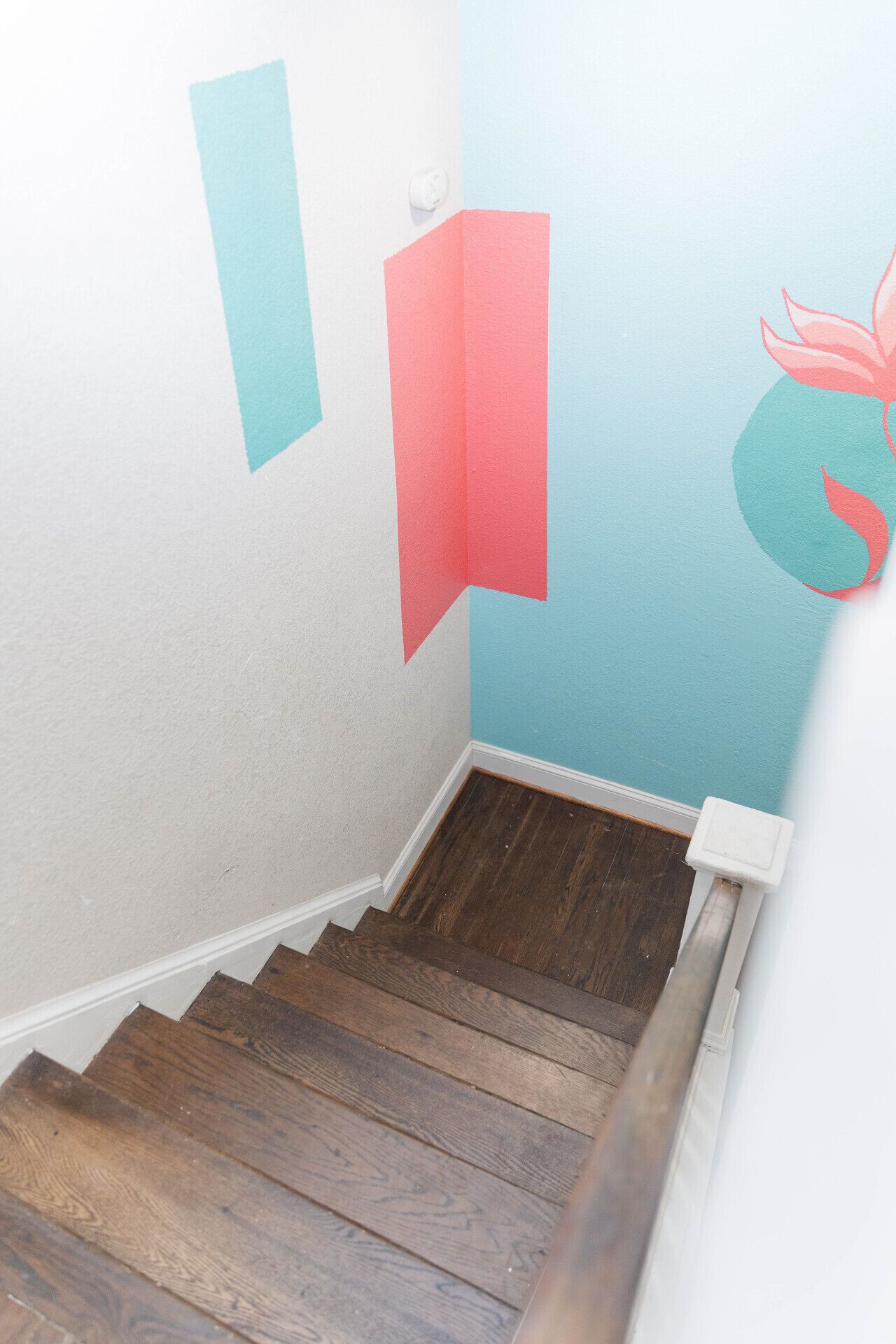 Een trap met houten treden en een witte muur met een ontwerp in teal en rood.