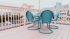 A balcony with teal chairs and a pink railing, overlooking a parking area and buildings.
