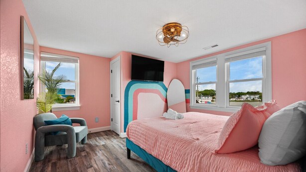 A bedroom with a bed, a chair, a desk, a mirror, and a window with a view.