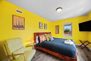 Una luminosa camera gialla con un letto, una sedia, una televisione e una finestra con vista.
