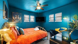 A bedroom with a bed, a ceiling fan, a TV, and a desk with a mirror.