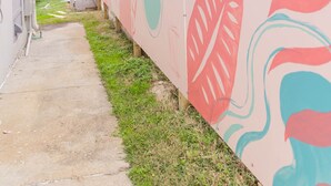 A narrow alleyway with a concrete path, a wooden fence, and a wall with abstract leaf patterns.