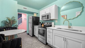 A kitchen with white cabinets, a stainless steel refrigerator, a microwave, an oven, and a sink with a gold faucet.
