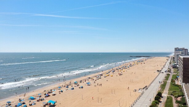 Ein weiter Sandstrand mit Sonnenschirmen und Menschen, ein klarer Himmel und Gebäude entlang der Küste.