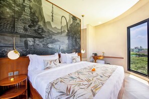 A modern hotel room with a large bed, a mural on the wall, a view of the city, and a wooden side table. - Villa Alinea (Tabanan)