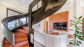 Un interior moderno con una escalera espiral, un sofá blanco y un televisor de pantalla plana.