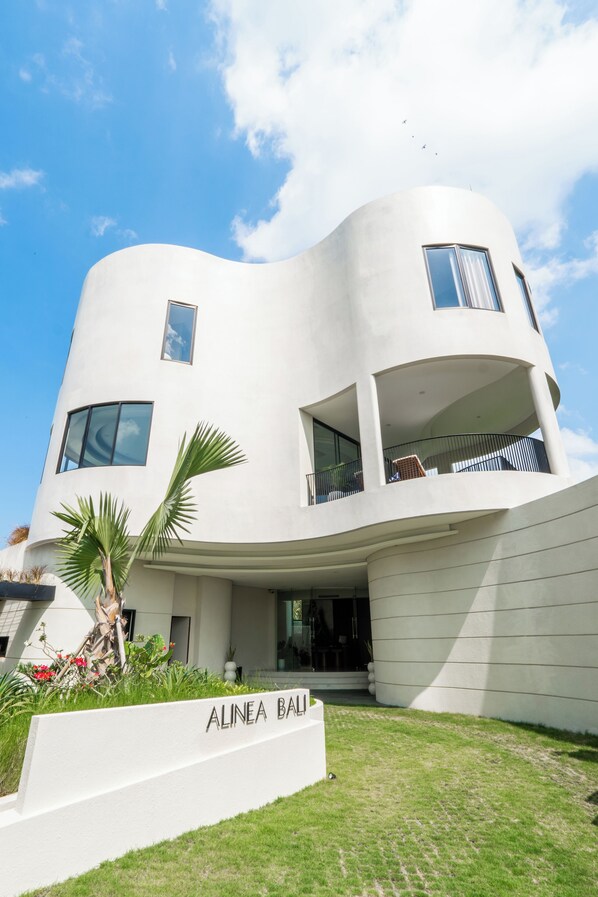 A modern, curved building with a white facade, large windows, and a balcony.