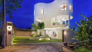 Una casa moderna de dos pisos con fachada curva, ventanas grandes y una entrada bien iluminada.