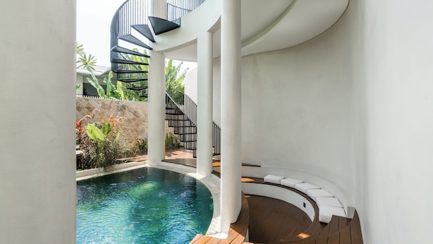 Un área de piscina interior moderna con una escalera de caracol, cubierta de madera y paredes blancas.
