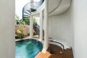 A modern indoor pool area with a spiral staircase, wooden deck, and white walls. - Villa Alinea (Tabanan)