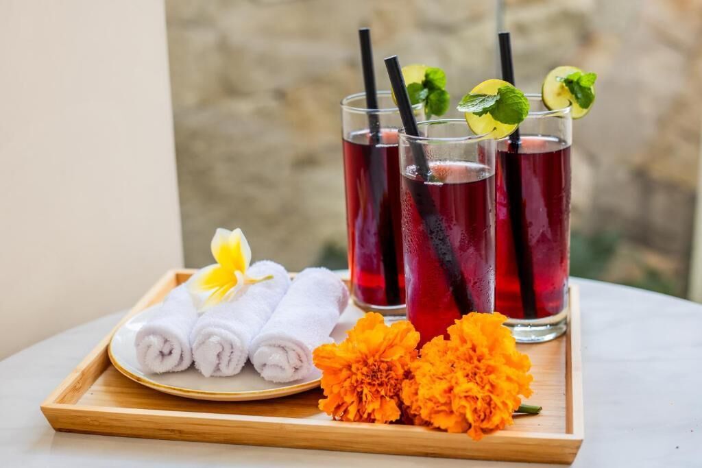 A tray with three glasses of red beverage, a plate with rolled towels, and a marigold flower.