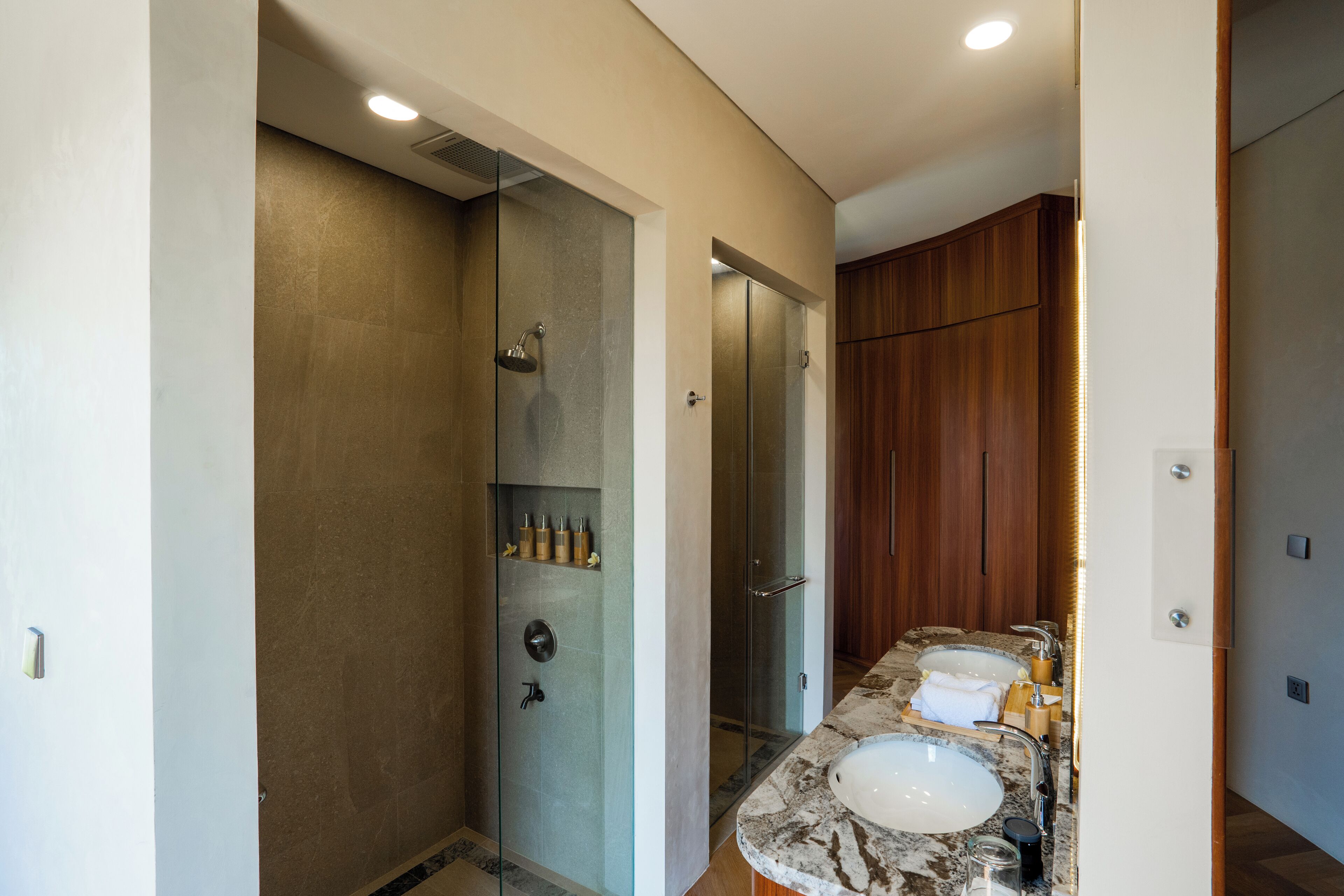 A modern bathroom with a glass-enclosed shower, two sinks, and wooden cabinets.