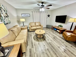 Ein Wohnzimmer mit einer Couch, einem Couchtisch, einem Fernseher und einem Deckenventilator.