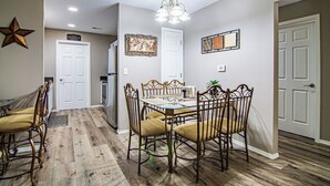 A dining area with a glass-top table, four chairs, a chandelier, and a star decoration on the wall.