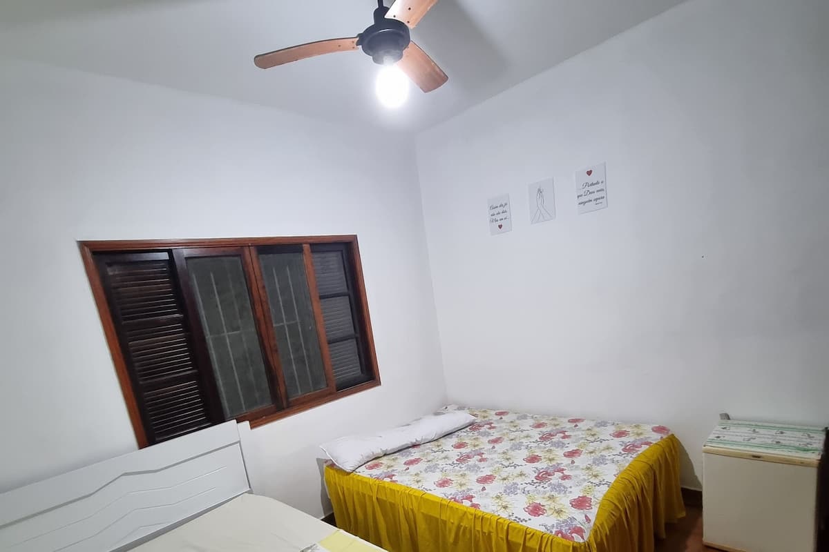 Ein Zimmer mit zwei Betten, einem Deckenventilator, einem Fenster mit Jalousien und einem kleinen Schrank.