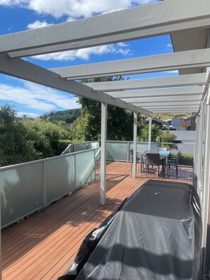 A covered outdoor deck with a table and chairs, surrounded by a wooden deck and metal railings.
