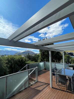 A covered outdoor area with a glass railing, a wooden deck, and a table with chairs.