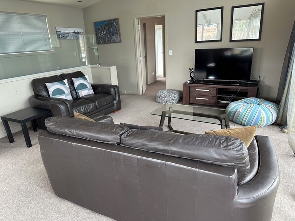 A modern living room with a leather sofa, a glass coffee table, a TV, and a bookshelf.
