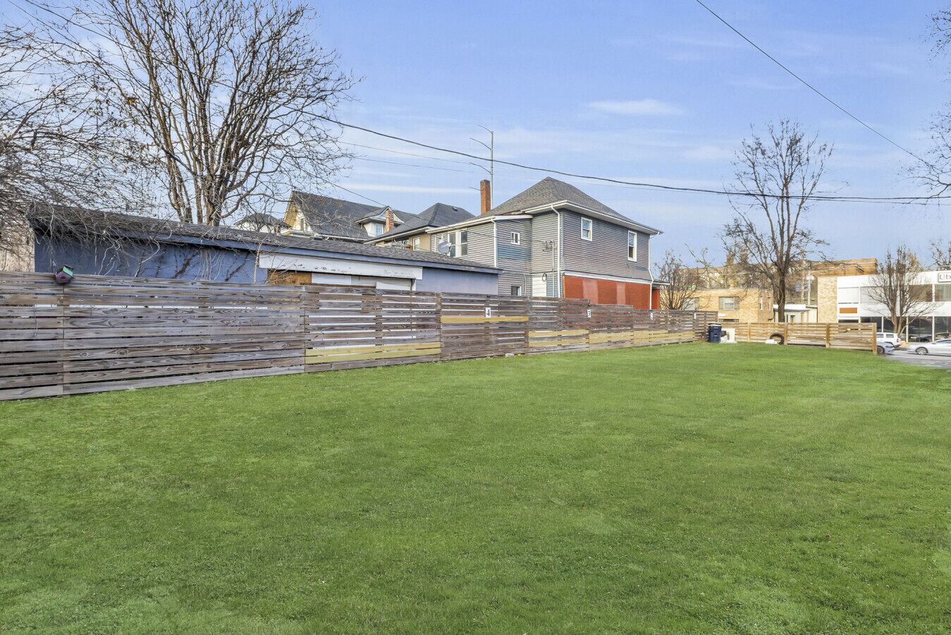 A residential backyard with a wooden fence, a grassy lawn, and houses in the background.