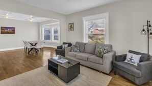 A modern living room with a grey sofa, a coffee table, and a dining area with a white table and chairs.