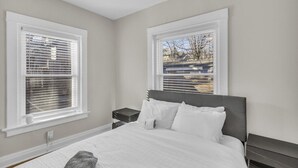 A bedroom with a bed, two bedside tables, and a window with blinds.