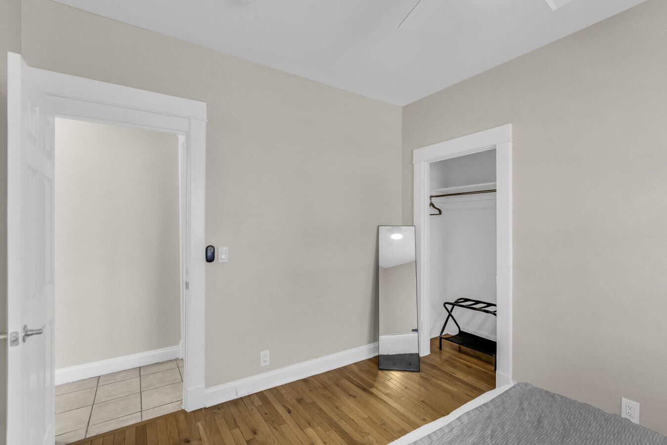 Una habitación con piso de madera, una puerta blanca, un espejo y un perchero.