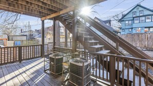 A covered outdoor area with a wooden deck, a staircase, and two air conditioning units.